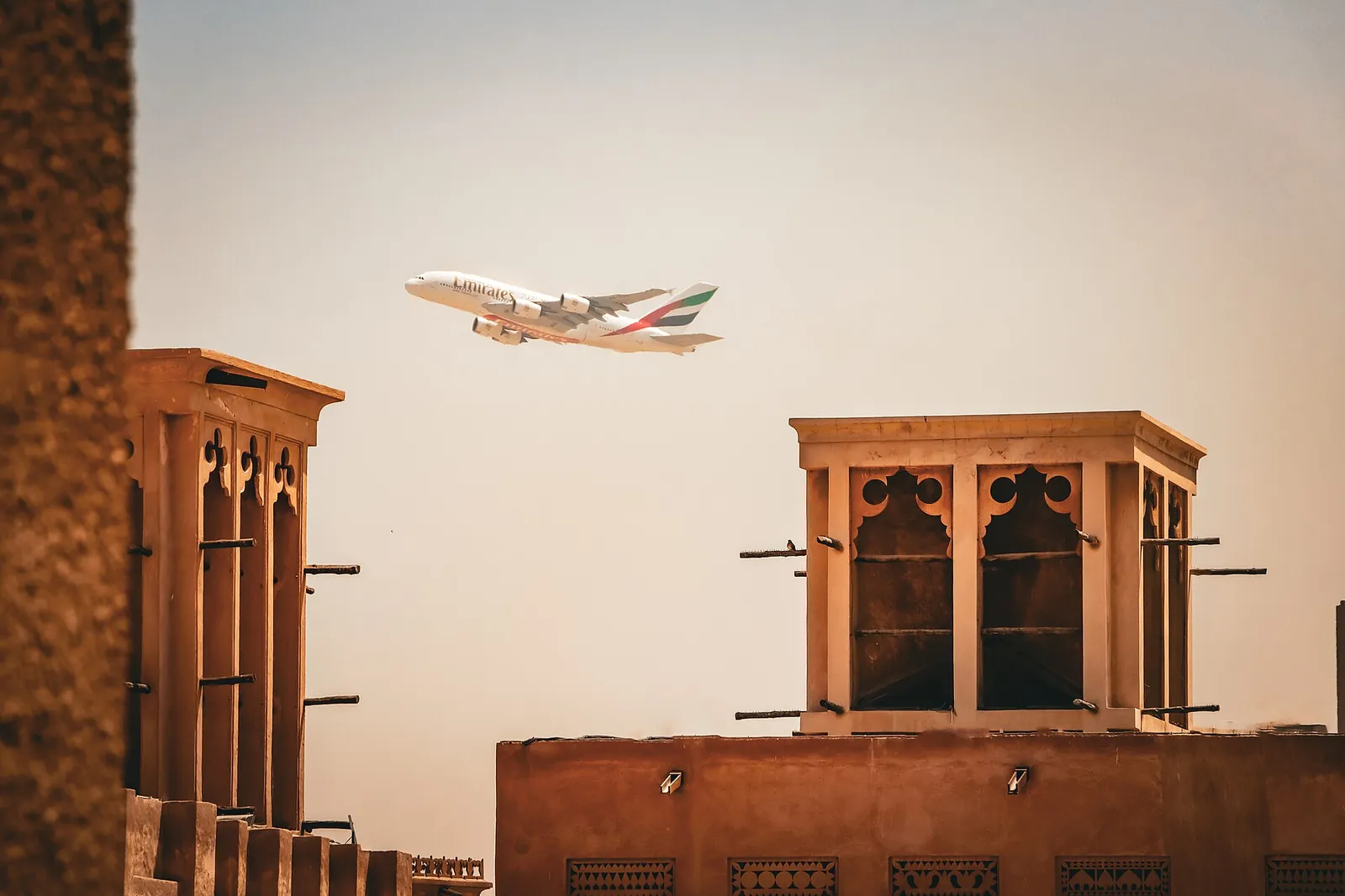 The Best Day in Dubai: A One-Day Itinerary With Every Dirham Counted 4 Wind towers of Al Fahidi Historical Neighbourhood in Dubai with a plane passing overhead